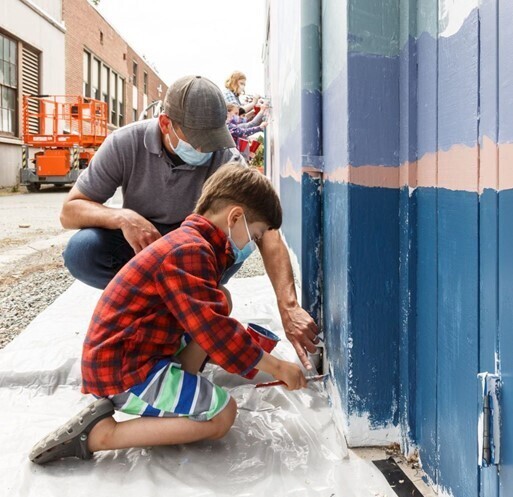 Artist Jeremy Jarvis assists a young child with painting a community mural. 